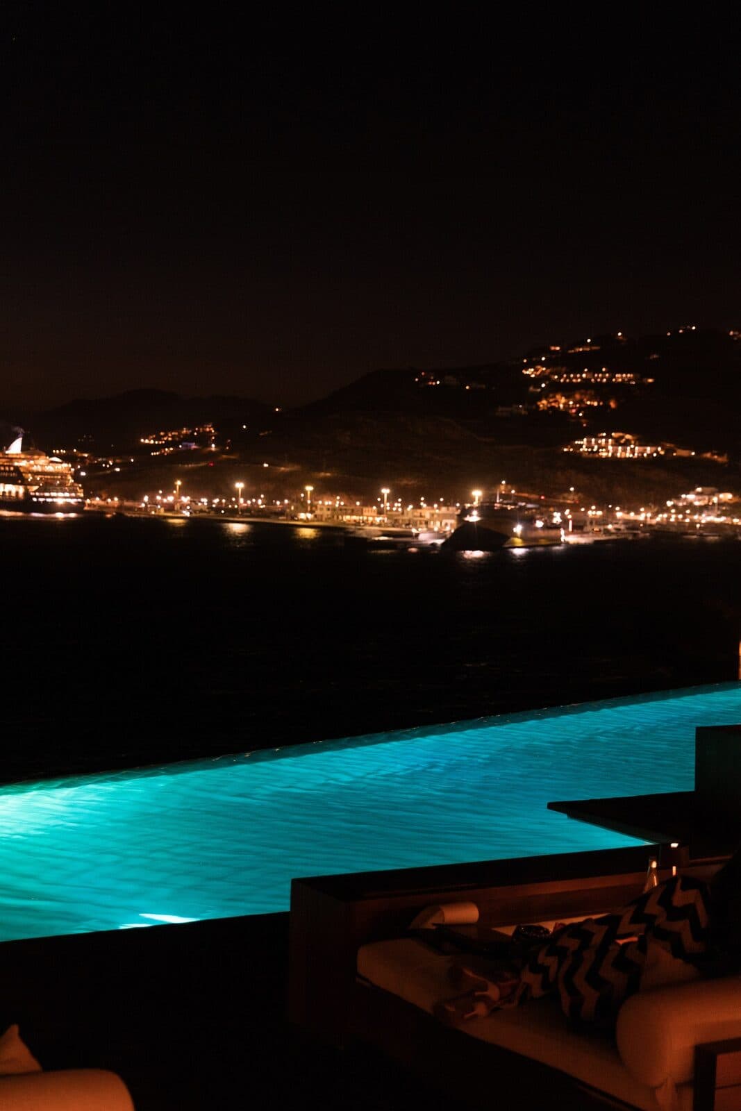 The infinity pool at night with Mykonos lights across the bay